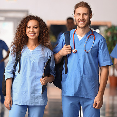 A young male and female nurse in scrubs with backpacks on.