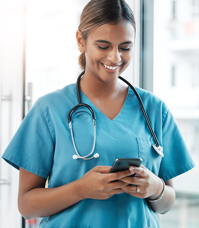 A smiling nurse in scrubs on her cell phone.