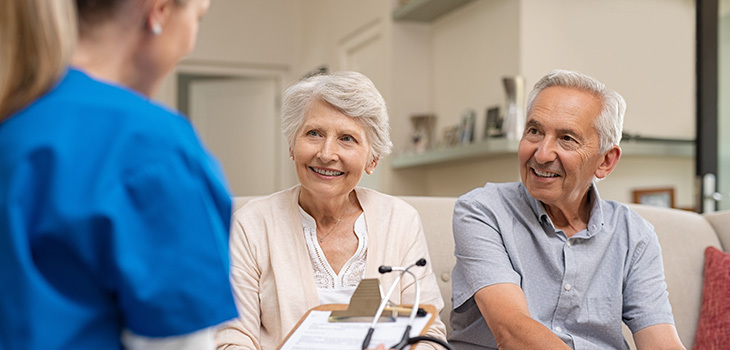 Two seniors speaking with a woman holding a clip board.