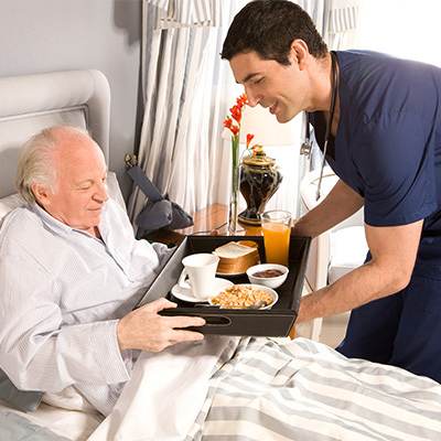 A nurse serving a try of food to a senior lying in bed.