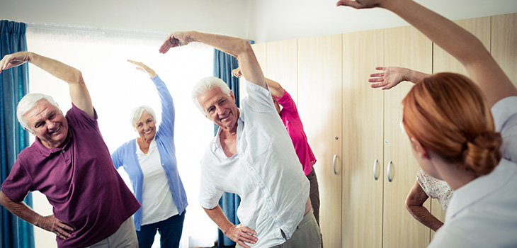 A group of seniors stretching in a room with an instructor.