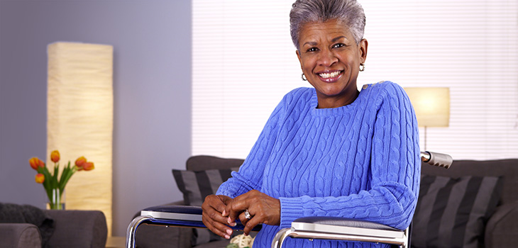 A senior in a wheelchair smiling in her room beside her couch.