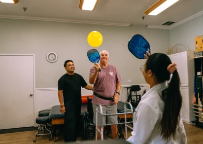 An elderly man hitting a balloon with a pickleball paddle at Casitas Care Center
