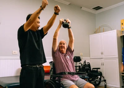 An elderly man lifting a weight above his head at Casitas Care Center