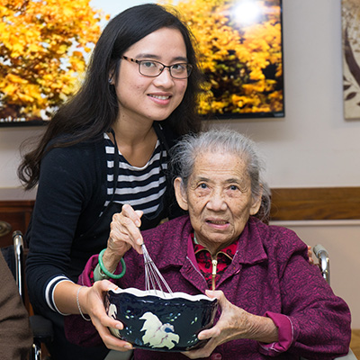 Staff member with an elderly resident serving food at the dining table.