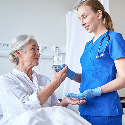 A nurse handing medication to a senior lying in bed.