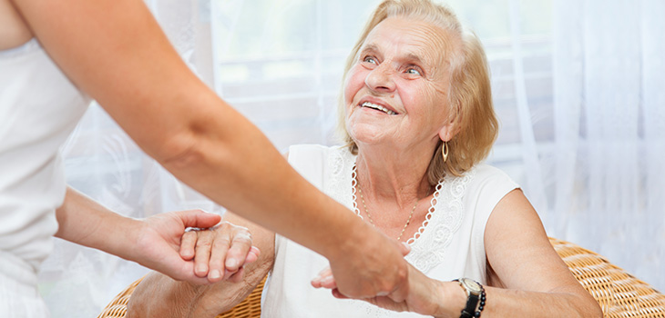 A woman helping a senior woman up out of her chair.