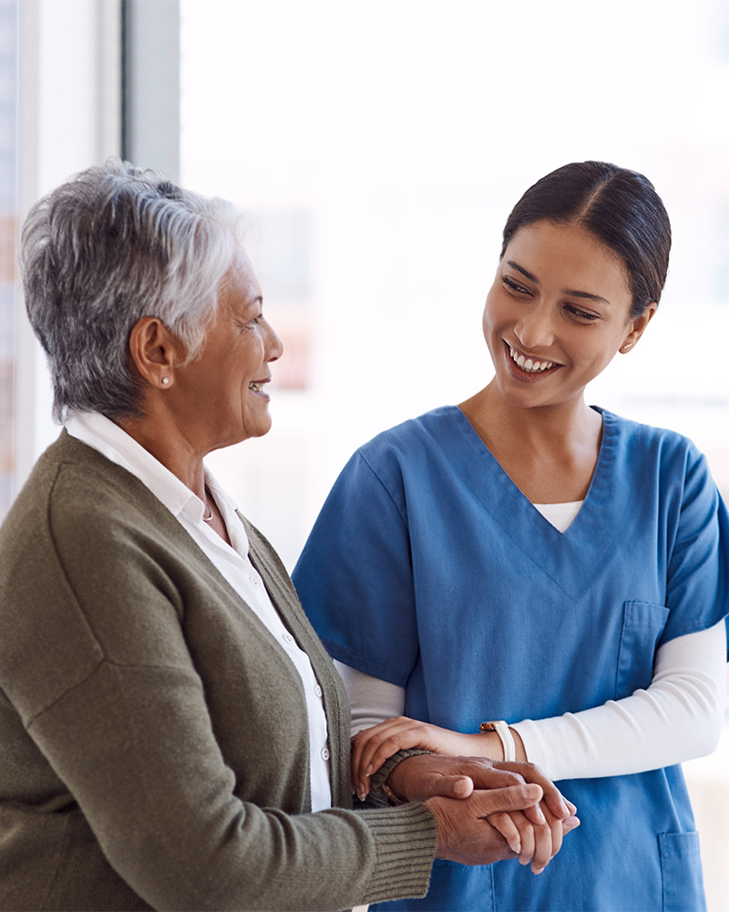A nurse and a mature woman walking arm-in-arm down a hallway.