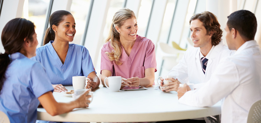 nurses and doctors sitting at a round table smiling and drinking coffee