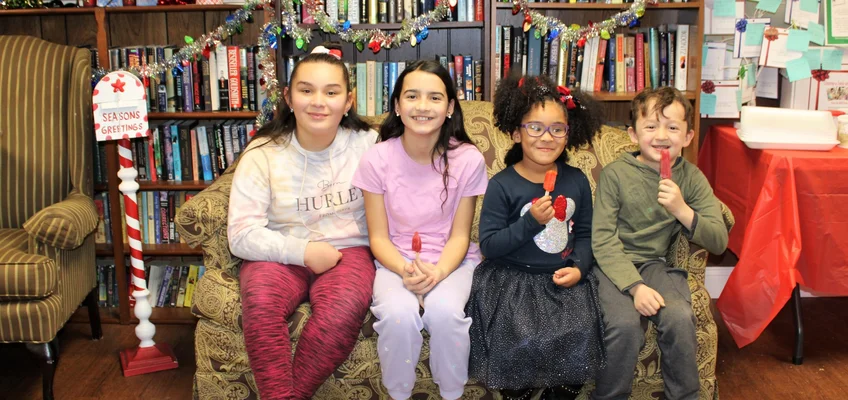 Four kids on sofa with Christmas decorations around them.