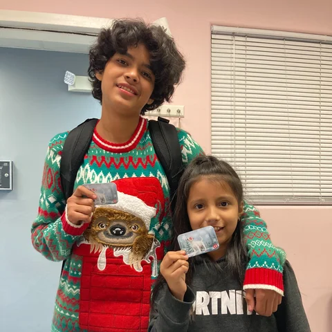 A boy in a christmas sweater and a younger girl both holding gift cards.