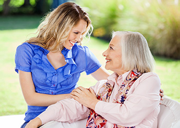 Two women smiling at each other outside.