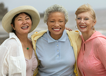 Three ladies standing arm-in-arm by the shore.