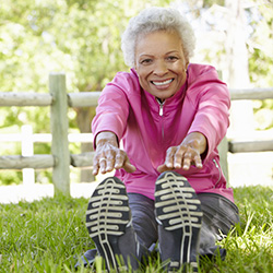 A senior stretching in grass beside a fence surrounded by trees.