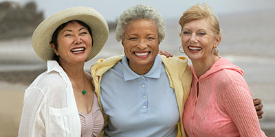 Three women standing on a beach together smiling.