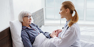 A nurse holding the hand of a patient lying in bed.