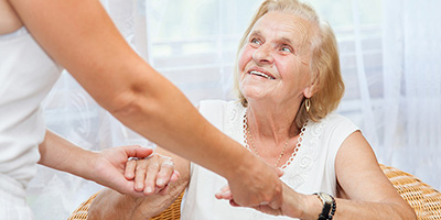 A woman helping a senior up out of her chair.