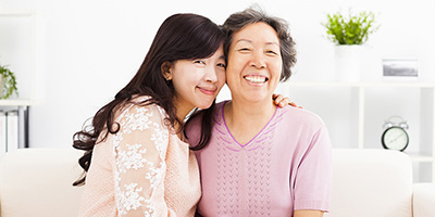 Two woman of asian descent on a couch embracing each other and smiling.