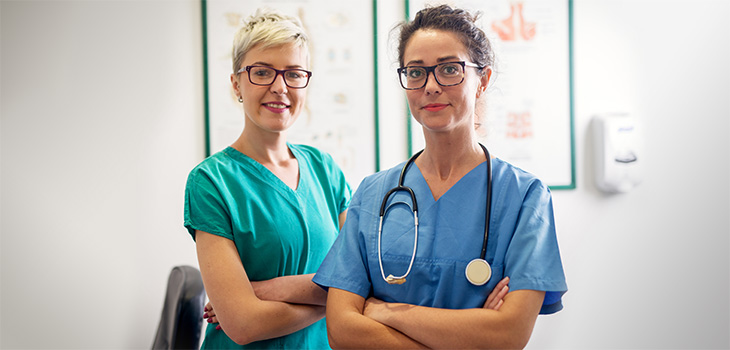 Two nurses standing together by a window smiling.